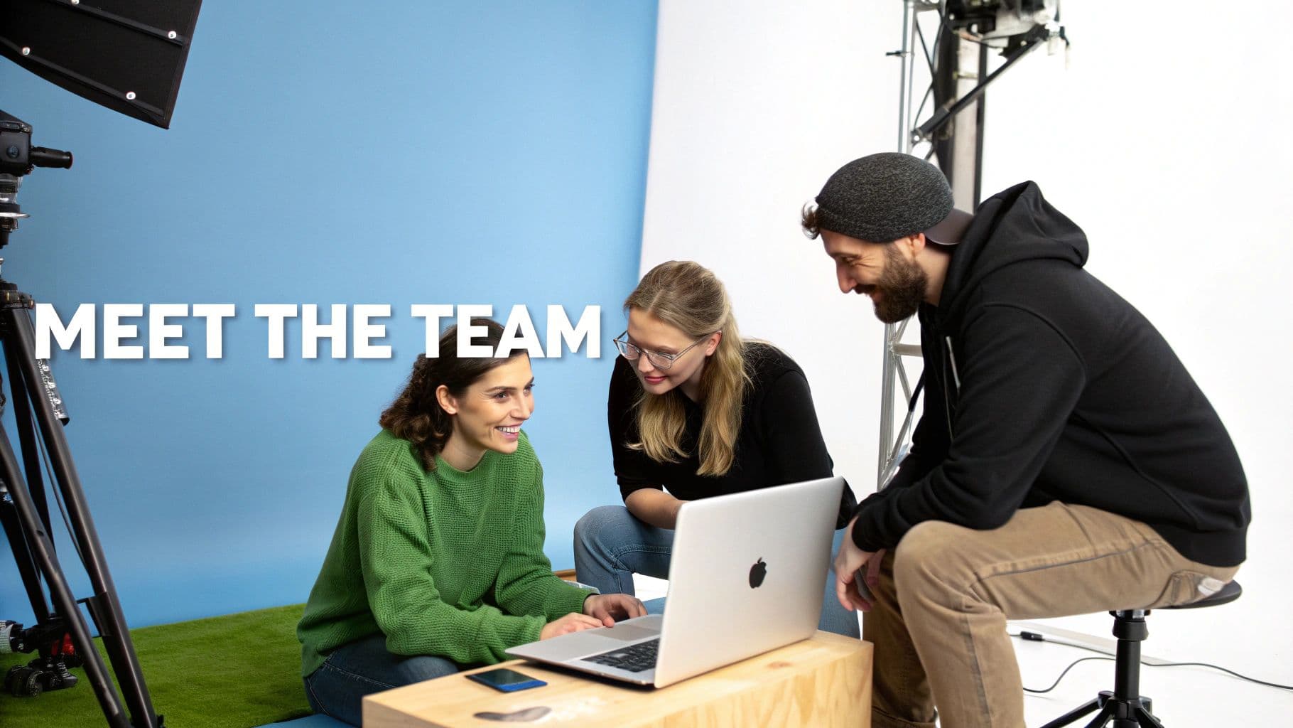 Smiling creative team collaborating on a laptop in a studio with camera equipment.